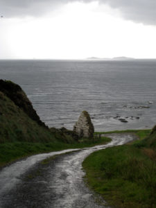 A dirt road in Ireland leading to the sea with a ruin. 