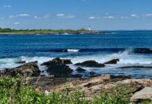 waves crashing on granite shoreline with lighthouse in background