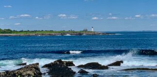 waves crashing on granite shoreline with lighthouse in background