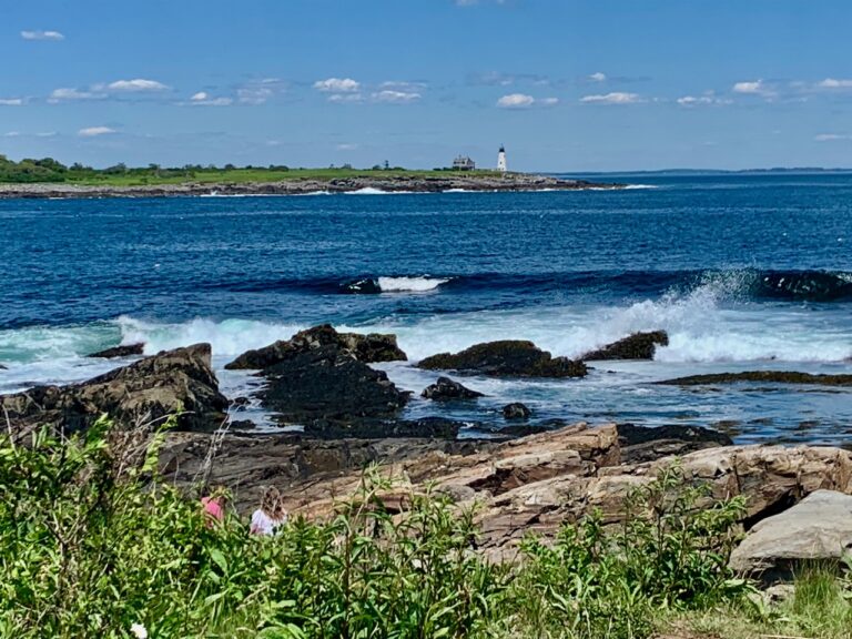waves crashing on granite shoreline with lighthouse in background
