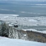 Image depicts a gondola over a trail at Le Massif with the St. Lawrence in the background. 